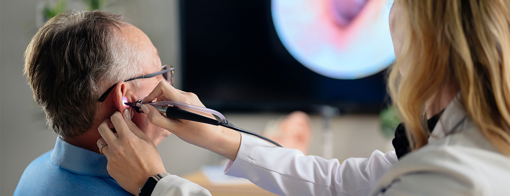 Image of hearing care professional using a hearing instrument to look inside a male patient's ear